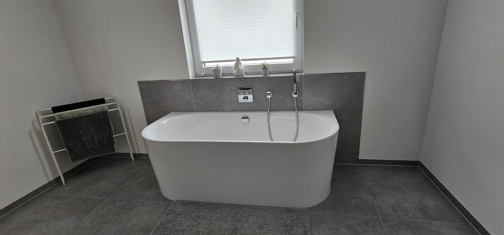 Freistehende Badewanne vor grauer Fliesenwand